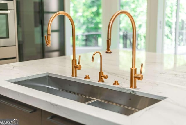 details featuring light stone counters, stainless steel oven, black fridge, and sink