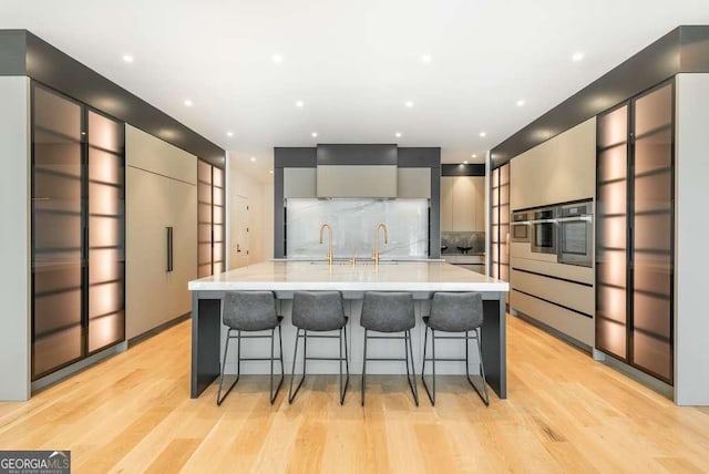 kitchen with a breakfast bar area, light hardwood / wood-style flooring, gray cabinetry, oven, and a large island with sink