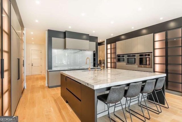 kitchen with gray cabinetry, a kitchen bar, light hardwood / wood-style floors, light stone countertops, and a spacious island