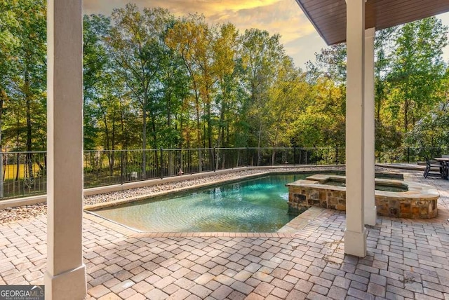 pool at dusk with an in ground hot tub and a patio