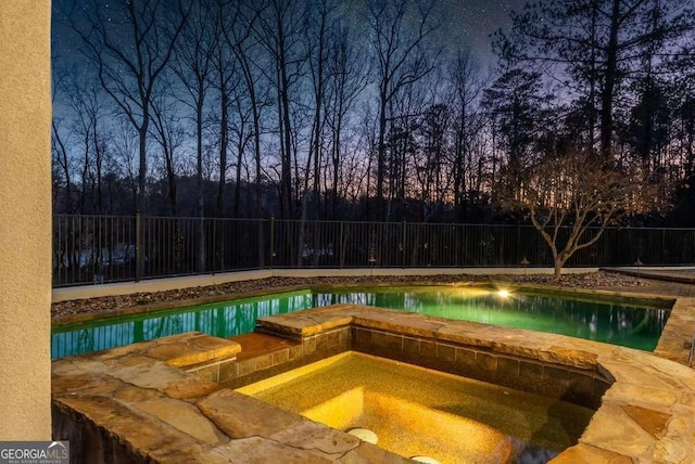 pool at dusk featuring an in ground hot tub