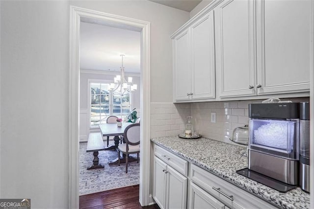 kitchen featuring tasteful backsplash, white cabinets, ornamental molding, light stone counters, and dark wood-type flooring