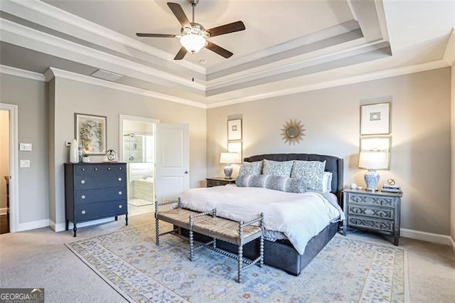 carpeted bedroom featuring a tray ceiling, ensuite bath, ornamental molding, and ceiling fan