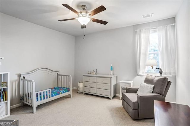 carpeted bedroom featuring ceiling fan and a crib