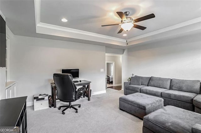 carpeted office space featuring ornamental molding, ceiling fan, and a tray ceiling