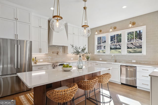 kitchen with a kitchen bar, appliances with stainless steel finishes, a kitchen island, pendant lighting, and white cabinets