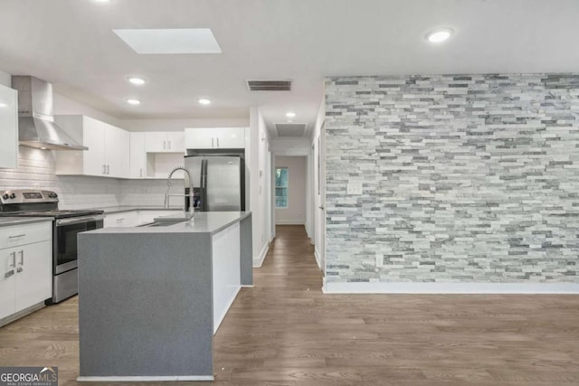 kitchen with appliances with stainless steel finishes, white cabinetry, sink, a kitchen island with sink, and wall chimney exhaust hood