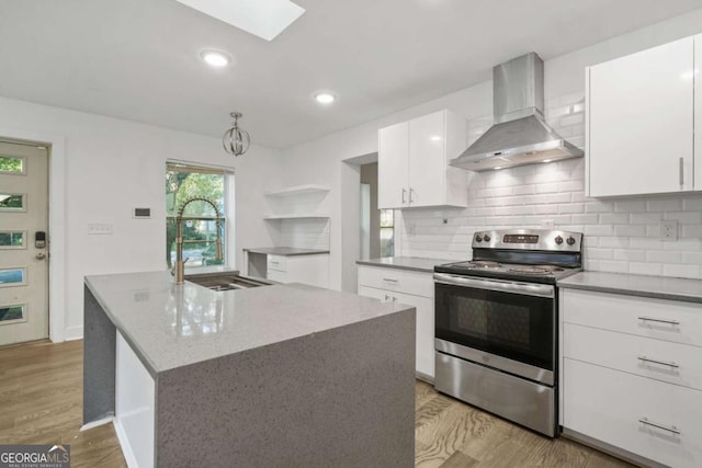 kitchen featuring an island with sink, white cabinets, light hardwood / wood-style floors, wall chimney range hood, and stainless steel electric range