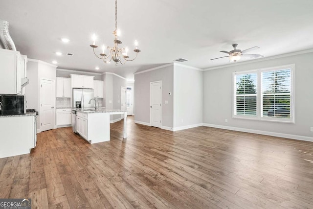 kitchen with hanging light fixtures, stainless steel refrigerator with ice dispenser, an island with sink, white cabinets, and light wood-type flooring