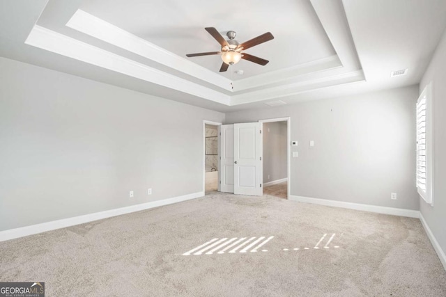 unfurnished bedroom with carpet floors, a raised ceiling, and ensuite bathroom