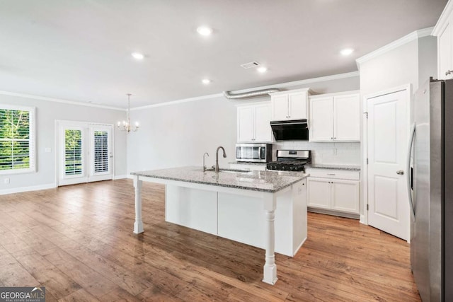 kitchen featuring appliances with stainless steel finishes, stone countertops, white cabinetry, a kitchen breakfast bar, and a kitchen island with sink