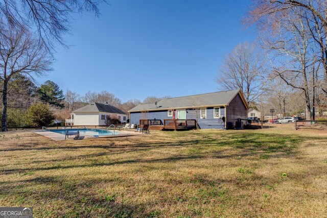 back of house with an outdoor pool, a yard, a wooden deck, and fence