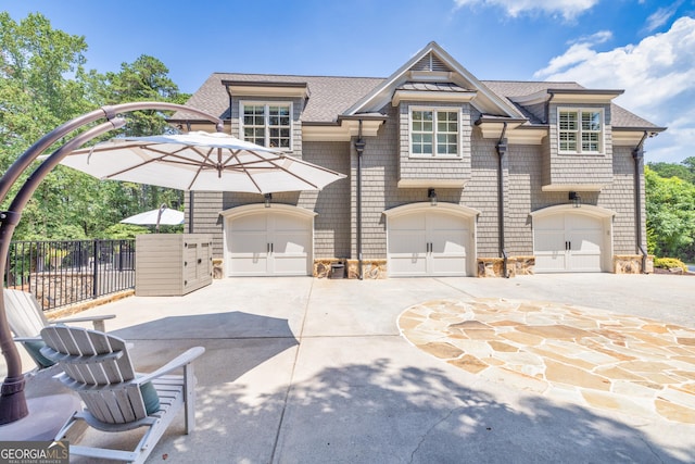 view of front of property featuring driveway, a shingled roof, stone siding, and fence