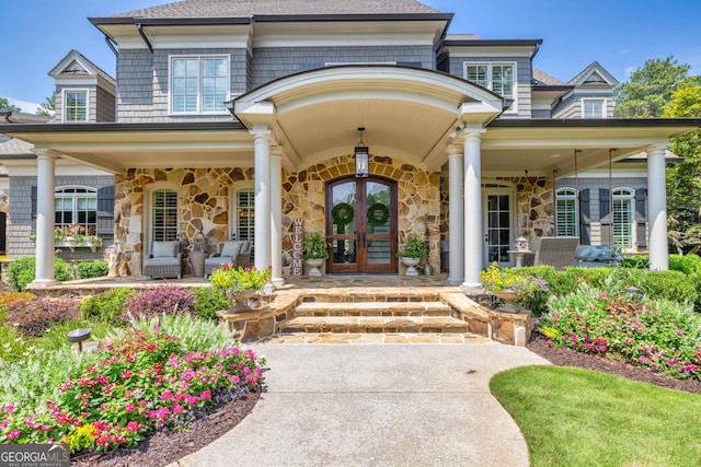 property entrance featuring stone siding, french doors, a porch, and a shingled roof