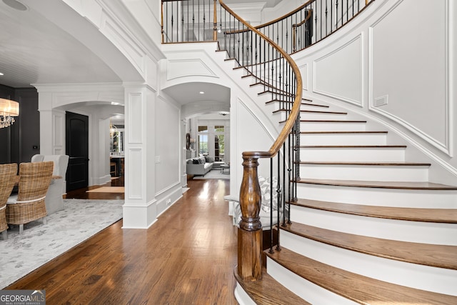 entryway with ornate columns, crown molding, dark wood-type flooring, and a notable chandelier