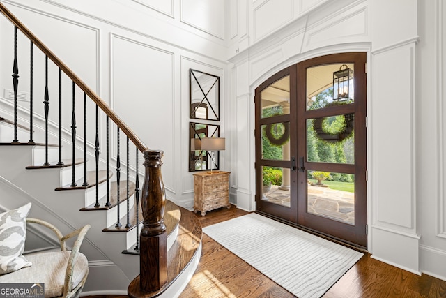 foyer entrance featuring arched walkways, a decorative wall, wood finished floors, and french doors