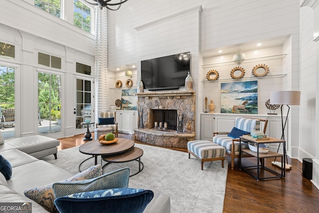 living room with a stone fireplace, dark wood-type flooring, and a towering ceiling