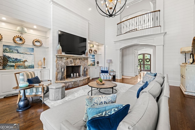 living area featuring a towering ceiling, arched walkways, wood finished floors, and a stone fireplace