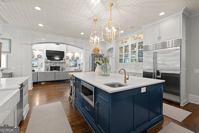 kitchen featuring blue cabinets, sink, white cabinetry, built in appliances, and decorative light fixtures