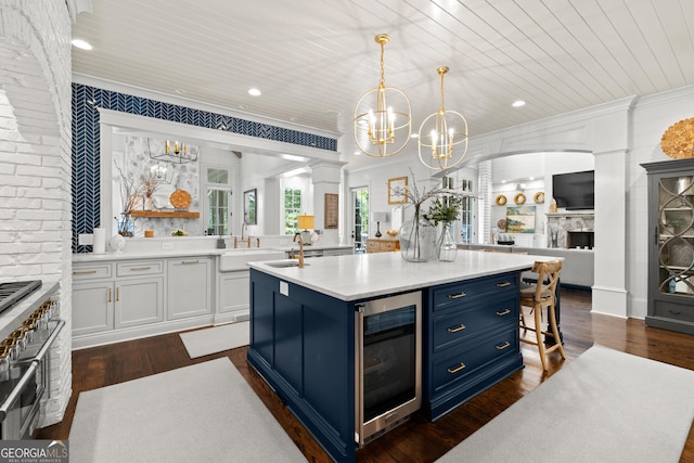 kitchen with wine cooler, blue cabinetry, white cabinetry, pendant lighting, and a kitchen island with sink