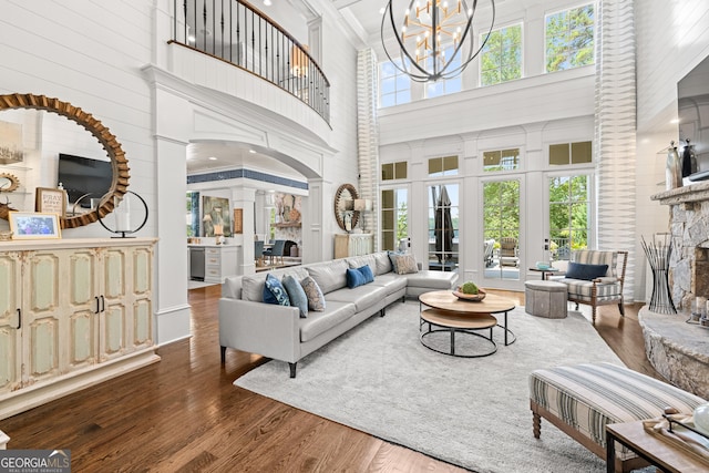 living room with a stone fireplace, dark hardwood / wood-style floors, a towering ceiling, decorative columns, and a chandelier