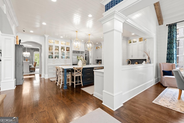 bar with arched walkways, a chandelier, stainless steel built in fridge, dark wood finished floors, and decorative columns