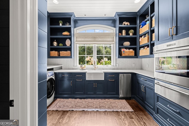 kitchen featuring blue cabinets, washer / dryer, sink, plenty of natural light, and oven