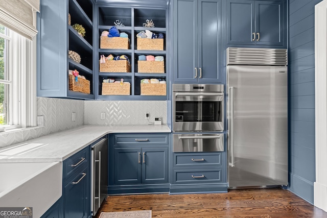 kitchen featuring blue cabinets, appliances with stainless steel finishes, dark hardwood / wood-style floors, and backsplash