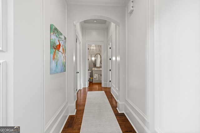 corridor with dark wood-style floors, arched walkways, crown molding, and a decorative wall