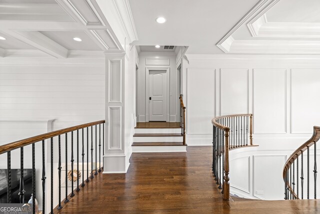 corridor featuring a decorative wall, wood finished floors, visible vents, an upstairs landing, and crown molding