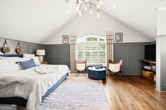 bedroom featuring a wainscoted wall, visible vents, a decorative wall, vaulted ceiling, and wood finished floors