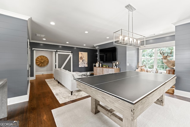 recreation room featuring crown molding, a barn door, dark hardwood / wood-style floors, and wooden walls