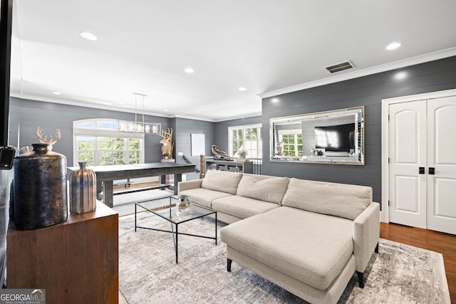 living area with a wealth of natural light, wood finished floors, visible vents, and crown molding