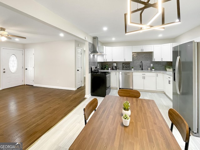 kitchen featuring appliances with stainless steel finishes, light hardwood / wood-style flooring, white cabinets, and wall chimney exhaust hood