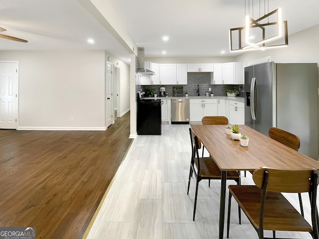 kitchen featuring pendant lighting, wall chimney range hood, white cabinetry, backsplash, and stainless steel appliances