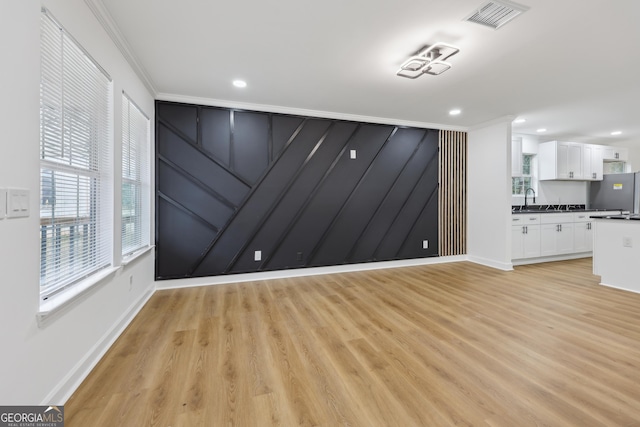 unfurnished living room with a sink, a healthy amount of sunlight, visible vents, and crown molding