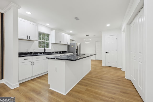 kitchen featuring a sink, white cabinets, light wood-type flooring, stainless steel refrigerator with ice dispenser, and a center island with sink