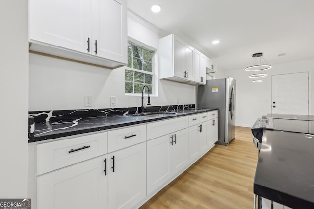 kitchen featuring light wood-type flooring, stainless steel fridge, a sink, and white cabinetry