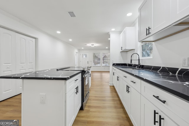 kitchen featuring visible vents, a kitchen island, light wood-style floors, a sink, and range with electric stovetop