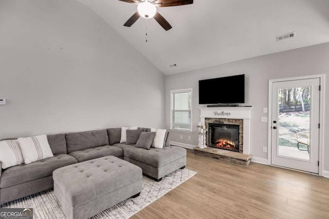 living room with ceiling fan, plenty of natural light, a stone fireplace, and light hardwood / wood-style flooring