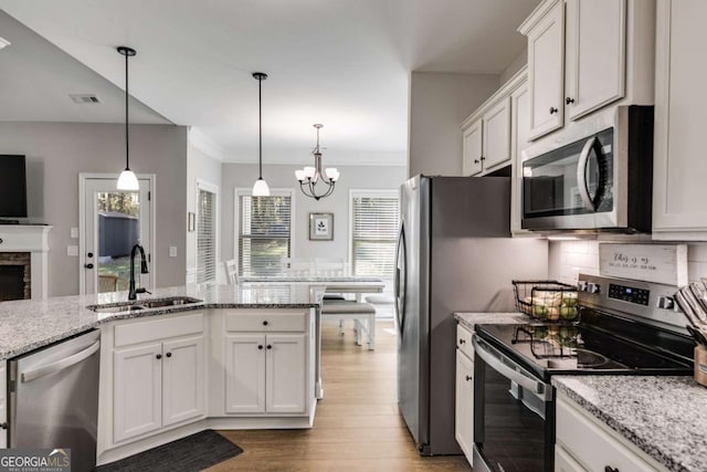 kitchen with sink, appliances with stainless steel finishes, hanging light fixtures, light stone counters, and white cabinets