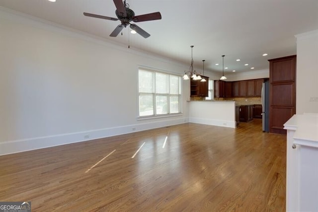 unfurnished living room featuring crown molding, ceiling fan with notable chandelier, and hardwood / wood-style floors