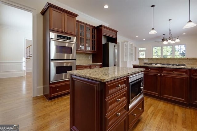 kitchen featuring crown molding, appliances with stainless steel finishes, a center island, light hardwood / wood-style floors, and decorative light fixtures