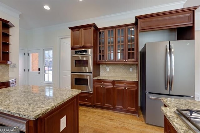 kitchen with ornamental molding, stainless steel appliances, light stone countertops, and light hardwood / wood-style flooring