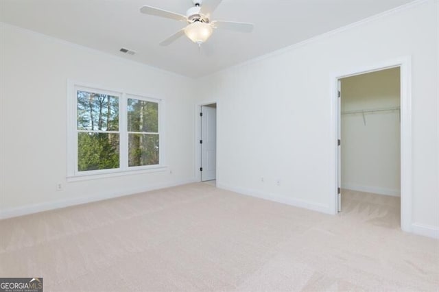 unfurnished bedroom with ornamental molding, a spacious closet, ceiling fan, light carpet, and a closet