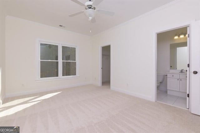 unfurnished bedroom featuring ensuite bathroom, sink, a walk in closet, light colored carpet, and crown molding