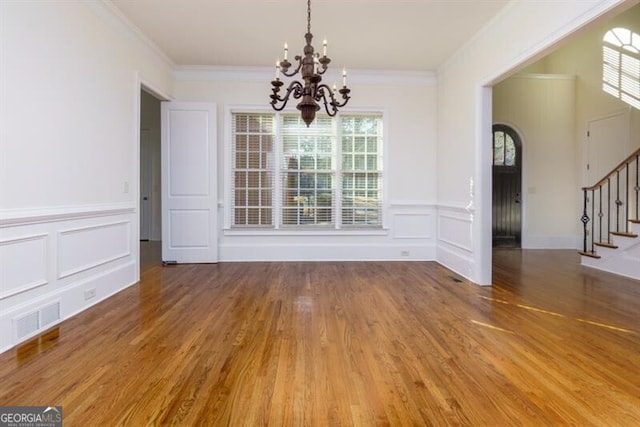 unfurnished dining area with wood-type flooring, ornamental molding, and a notable chandelier