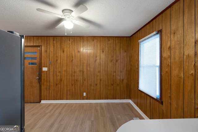 unfurnished bedroom with stainless steel fridge, a textured ceiling, multiple windows, and light wood-type flooring