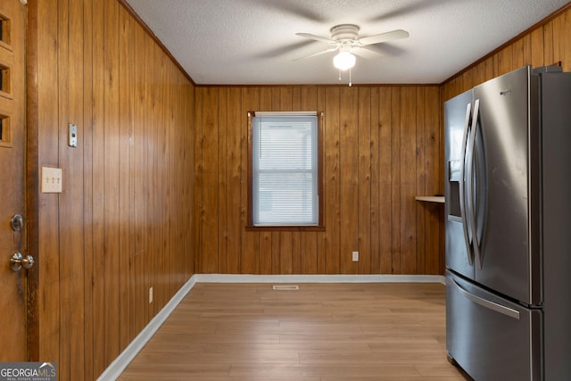 kitchen with stainless steel fridge, ceiling fan, wooden walls, a textured ceiling, and light wood-type flooring