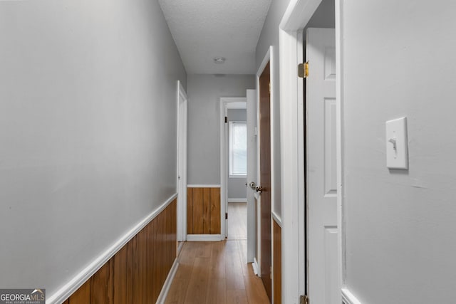 corridor with wood walls, a textured ceiling, and light wood-type flooring